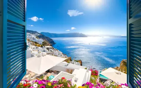 Vista mozzafiato su Santorini, perfetta per sapere dove andare in vacanza a giugno. Case bianche a picco sul mare blu intenso, fiori colorati e sole splendente.