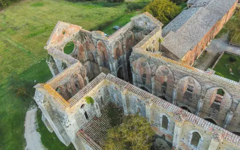 Rovine suggestive dell'abbazia nel Val di Merse, con archi gotici e tetti in tegole rosse, immerse nel verde della campagna toscana.