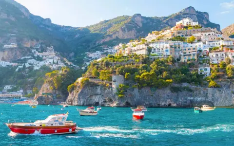 Barche a vela solcano le acque turchesi, con case colorate aggrappate alle scogliere dei paesi della costiera amalfitana.