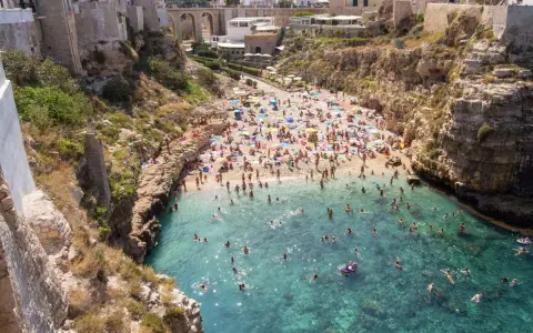 Spiaggia affollata e mare cristallino a Polignano a Mare. Ecco cosa fare: godersi il sole, nuotare e rilassarsi tra le scogliere.