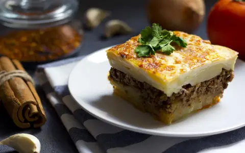 Un assaggio di cosa mangiare ad Atene: moussaka fatta in casa, con strati di patate, carne macinata e besciamella dorata, guarnita con prezzemolo fresco.