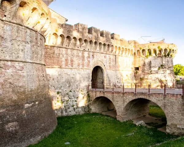 Antiche mura di Colle Val d'Elsa con un ponte ad arco che conduce a un portone fortificato.