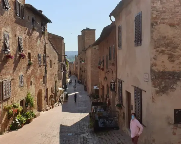 Un vicolo medievale a Certaldo, cosa vedere: case in mattoni, finestre con persiane, fiori e un uomo con mascherina.
