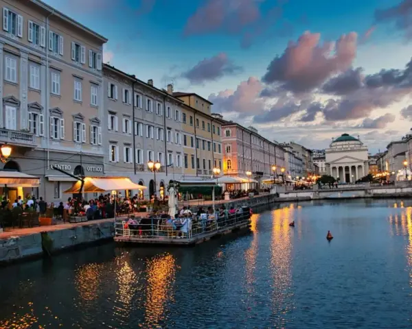 Serata magica a Trieste, uno dei tanti posti belli in Italia. Canale illuminato, palazzi storici e gente ai tavolini all'aperto.