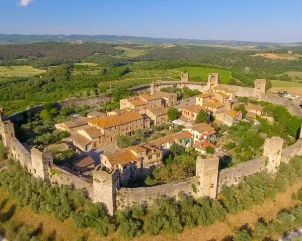 Borgo medievale fortificato nella valle del Chianti, con torri e mura antiche immerse nel verde della campagna toscana.