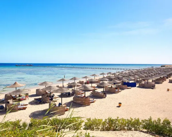 Spiaggia di Marsa Alam con file di ombrelloni e lettini, molo sull'acqua cristallina. Ideale per escursioni e relax.