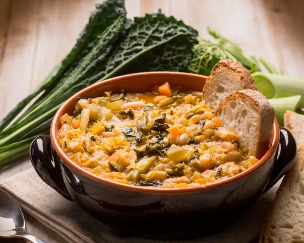 Zuppa di verdure e fagioli, un classico dei cibi tipici toscani, servita con pane rustico e contornata da cavolo nero.