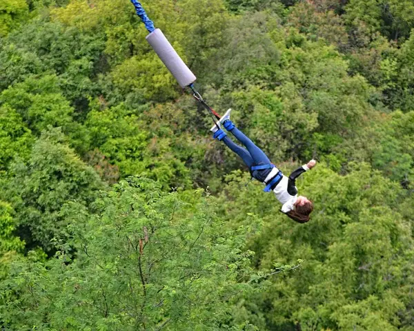Donna in caduta libera durante un'emozionante esperienza di bungee jumping in Italia, circondata da una lussureggiante foresta verde.