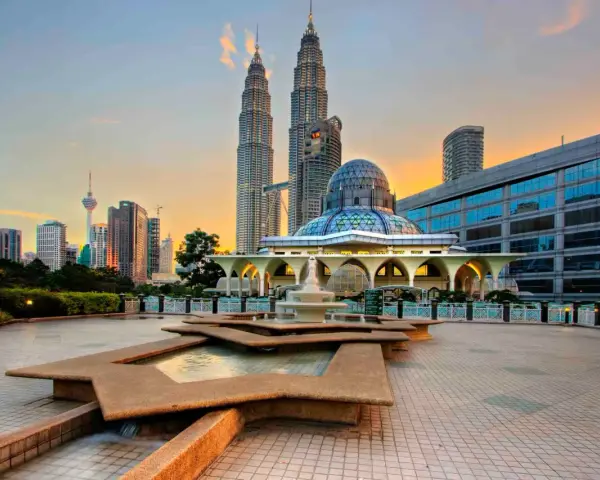 Le Petronas Towers dominano lo skyline di Kuala Lumpur, con una moschea moderna e fontane in primo piano. Un'ottima vista di cosa vedere a Kuala Lumpur al tramonto.