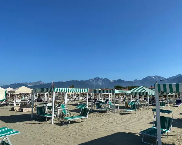 Spiaggia attrezzata a Marina di Pietrasanta con lettini e ombrelloni a righe verdi e bianche, sullo sfondo le montagne.