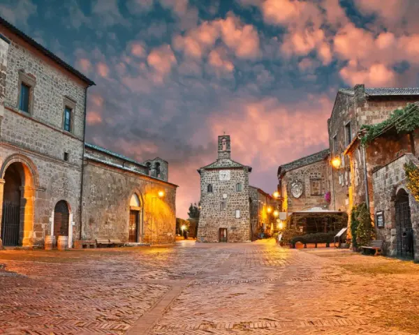 Piazza medievale illuminata al tramonto, con edifici in pietra e un campanile. Un luogo incantevole dove scoprire cosa vedere.