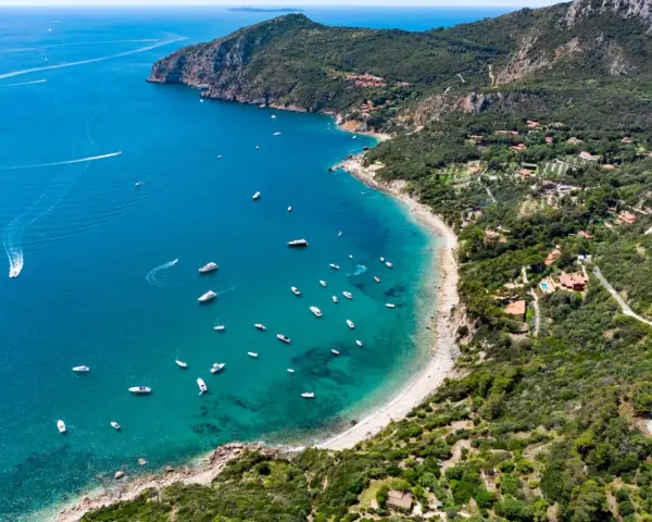 Baia con acque cristalline e numerose barche, incastonata nella costa verdeggiante dell'Argentario, dove si trova un paradiso naturale.