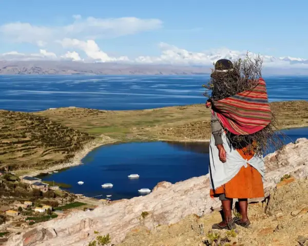 Donna indigena con fascina di legna, vista sul Lago Titicaca, un luogo imperdibile da vedere in Bolivia.
