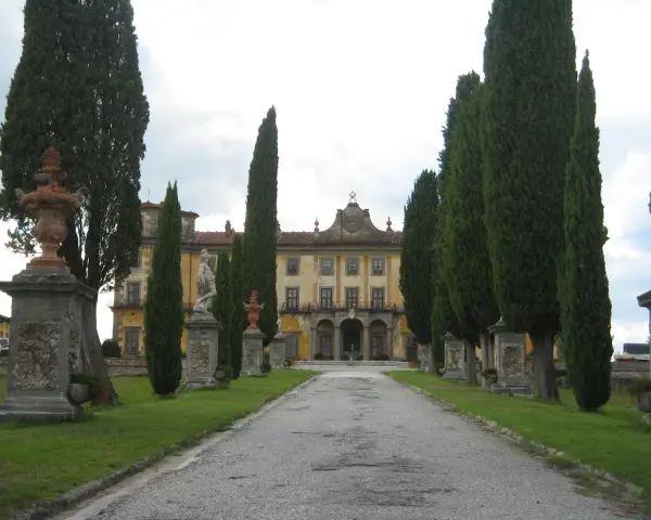 Viale alberato conduce a un palazzo giallo, con statue e fontane, tipico di un borgo a Buggiano.