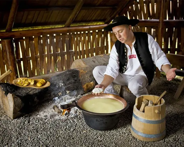 Uomo in abito tradizionale polacco prepara un prodotto tipico della Polonia: formaggio in un paiolo di rame.