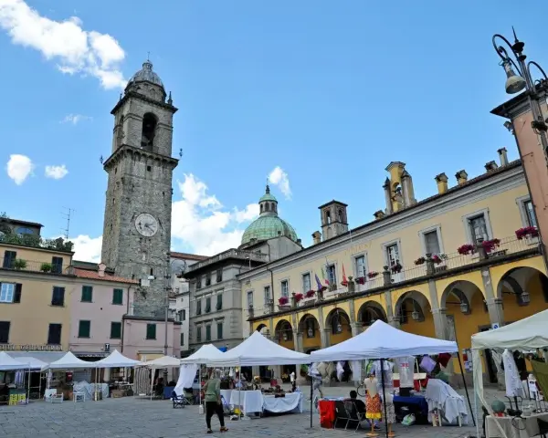 Mercato in piazza a Pontremoli, con la torre civica e il palazzo del Comune. Ecco cosa vedere a Pontremoli: un'atmosfera vivace.