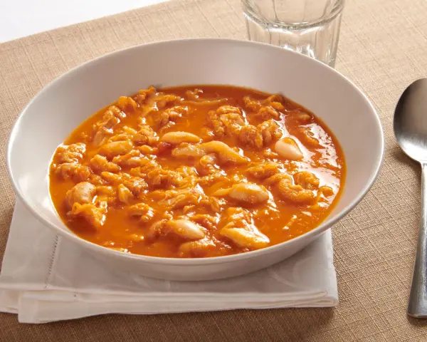 Piatto tipico pisano: trippa alla pisana in un bianco piatto, servita con forchetta e cucchiaio.