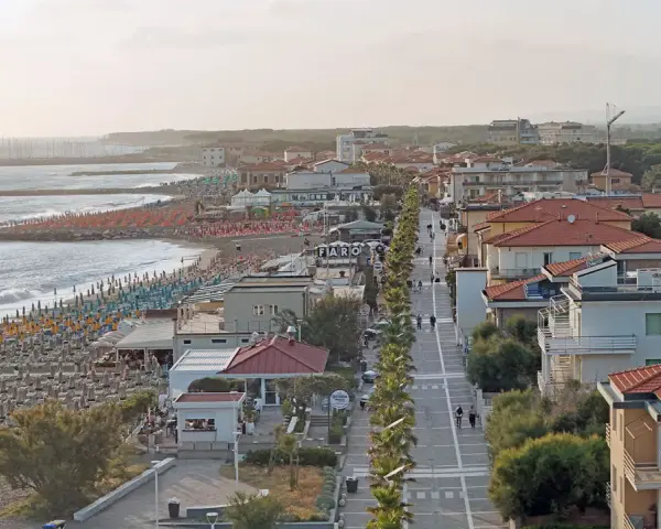 Vista aerea del lungomare di Marina di Cecina con spiaggia attrezzata, mare calmo e case con tetti rossi.