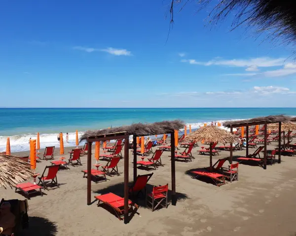 Spiaggia attrezzata a Marina di Bibbona con lettini rossi, ombrelloni di paglia e il mare azzurro sullo sfondo.
