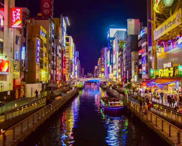 Un canale illuminato da insegne al neon a Osaka, cosa vedere: un tour in battello tra edifici vibranti e riflessi sull'acqua.
