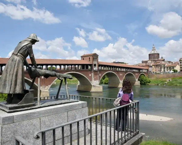 Pavia cosa vedere in un giorno: il Ponte Coperto con la statua della lavandaia e la cupola del Duomo sullo sfondo.