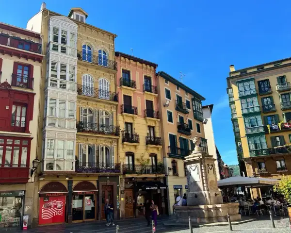 Edifici colorati con balconi in ferro battuto e una fontana in una piazza. Perfetto per scoprire cosa vedere a Bilbao in 3 giorni.