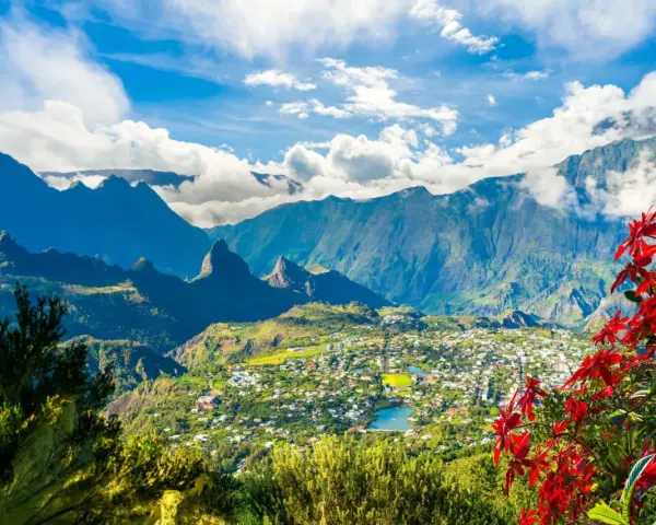 Vista panoramica di un villaggio verdeggiante sull'isola di Reunion, incastonato tra imponenti montagne blu e fiori rossi vibranti.
