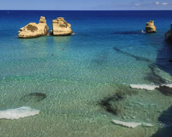 Un mare bello in Italia, con scogli dorati che emergono da acque cristalline e turchesi. Alcune persone nuotano in questo paradiso.