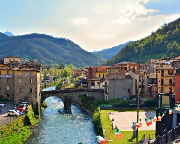 Un pittoresco scorcio di Castelnuovo di Garfagnana con il fiume Serchio che attraversa il borgo, circondato da colline verdi.