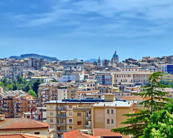 Panoramica di **Caltanissetta cosa vedere**: tetti rossi, palazzi colorati e la cupola di una chiesa sotto un cielo azzurro.