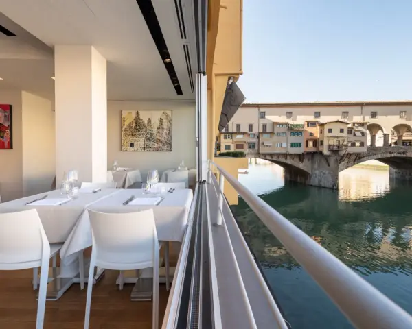 Tavoli apparecchiati in un ristorante con vista su Ponte Vecchio. Un'ottima opzione per sapere dove mangiare a Firenze.