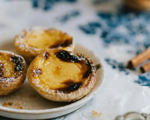 Pastéis de nata, un must per sapere cosa mangiare a Porto. Dolci cremosi su un piatto, spolverati di zucchero a velo, con cannella sullo sfondo.