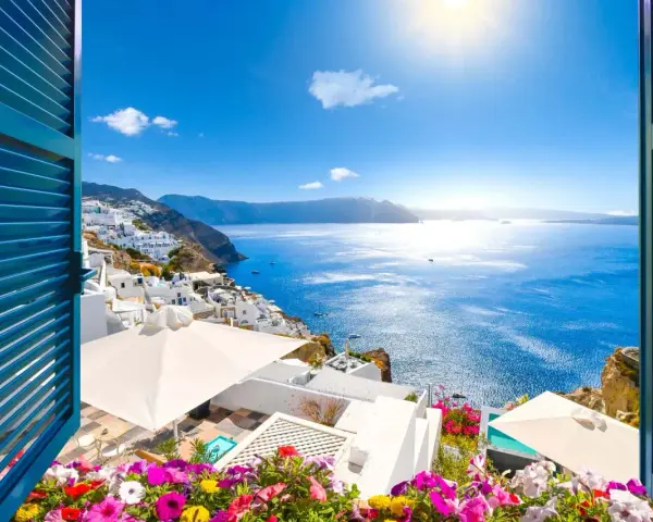 Vista mozzafiato su Santorini, perfetta per sapere dove andare in vacanza a giugno. Case bianche a picco sul mare blu intenso, fiori colorati e sole splendente.