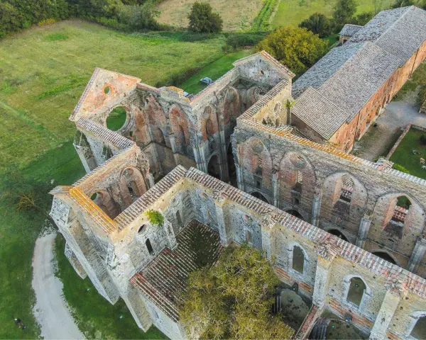 Rovine suggestive dell'abbazia nel Val di Merse, con archi gotici e tetti in tegole rosse, immerse nel verde della campagna toscana.
