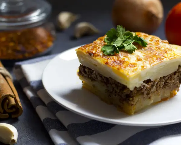 Un assaggio di cosa mangiare ad Atene: moussaka fatta in casa, con strati di patate, carne macinata e besciamella dorata, guarnita con prezzemolo fresco.