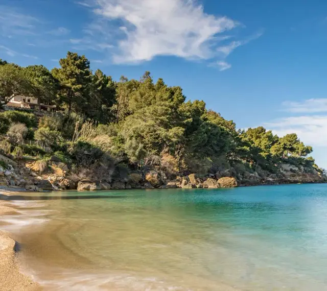 Spiaggia tranquilla con acque cristalline e una villa immersa nel verde sulla costa di Castellammare del Golfo.