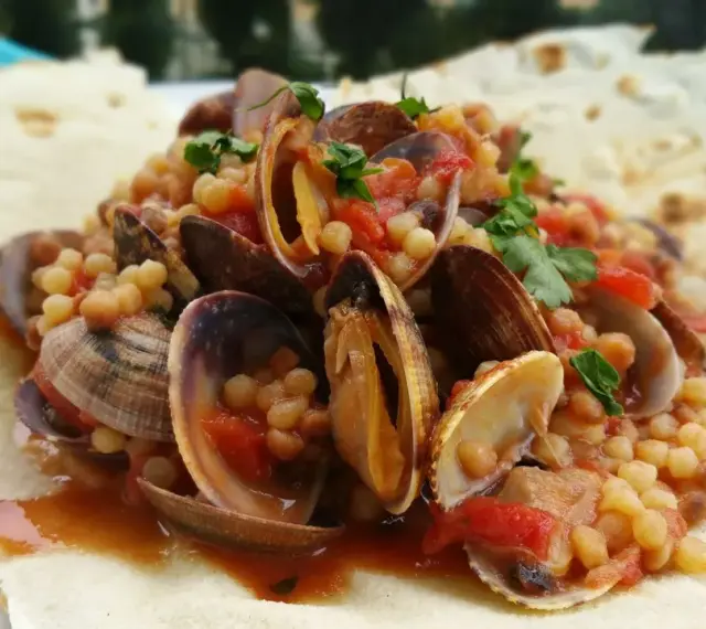 Vongole e fregola, un classico dei piatti tipici sardi, servite su pane carasau croccante.