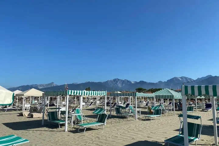 Spiaggia attrezzata a Marina di Pietrasanta con lettini e ombrelloni a righe verdi e bianche, sullo sfondo le montagne.