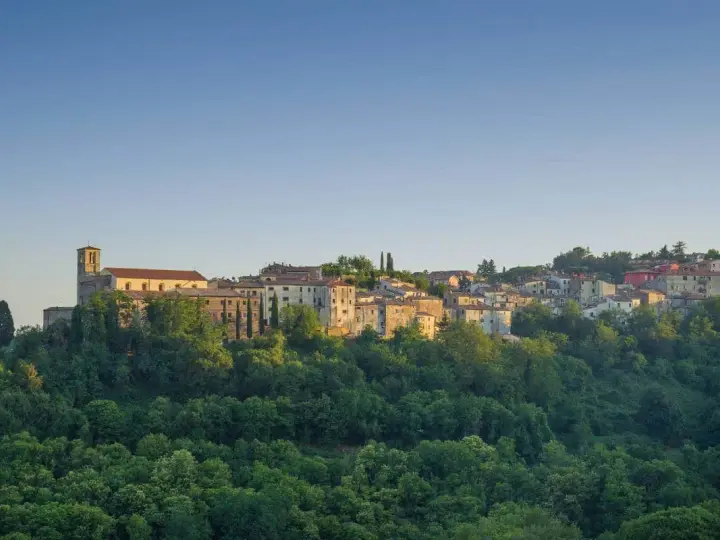 Borgo collinare con chiesa e case in pietra, immerso nel verde. Un luogo incantevole dove scansano cosa vedere, tra storia e natura.