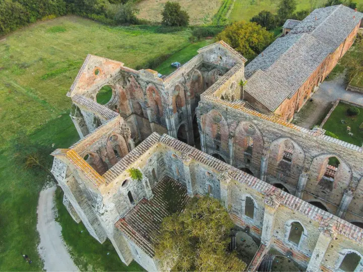 Rovine suggestive dell'abbazia nel Val di Merse, con archi gotici e tetti in tegole rosse, immerse nel verde della campagna toscana.