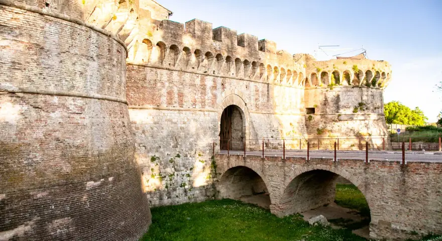 Antiche mura di Colle Val d'Elsa con un ponte ad arco che conduce a un portone fortificato.