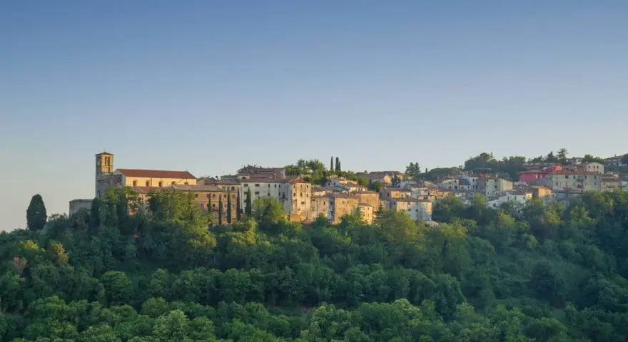 Borgo collinare con chiesa e case in pietra, immerso nel verde. Un luogo incantevole dove scansano cosa vedere, tra storia e natura.