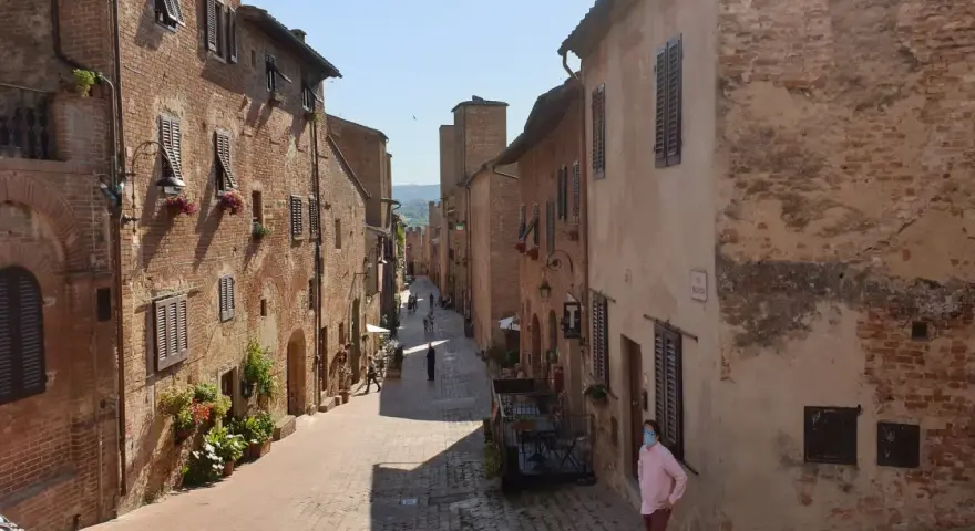 Un vicolo medievale a Certaldo, cosa vedere: case in mattoni, finestre con persiane, fiori e un uomo con mascherina.
