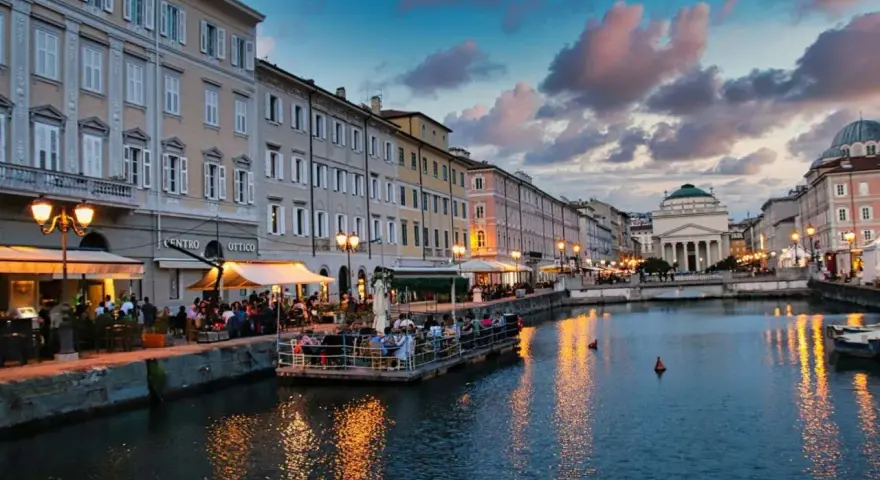 Serata magica a Trieste, uno dei tanti posti belli in Italia. Canale illuminato, palazzi storici e gente ai tavolini all'aperto.