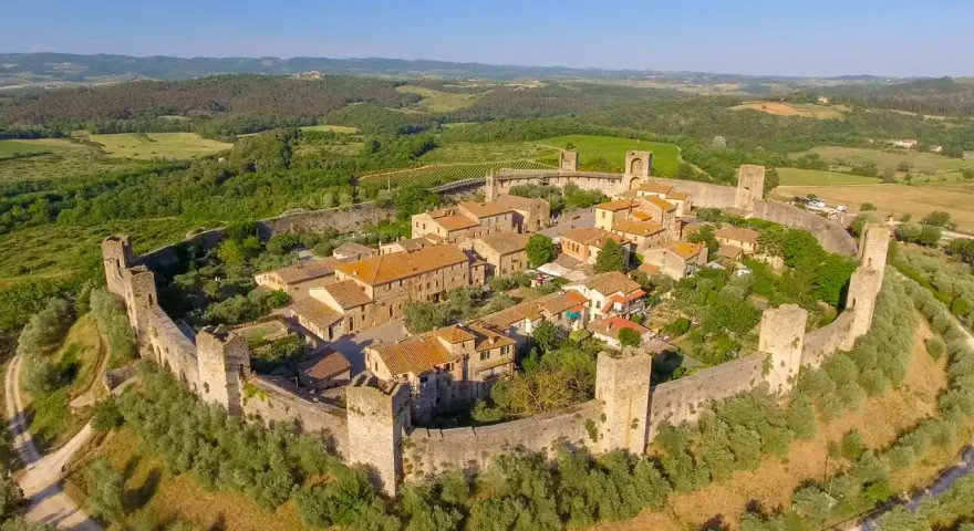 Borgo medievale fortificato nella valle del Chianti, con torri e mura antiche immerse nel verde della campagna toscana.