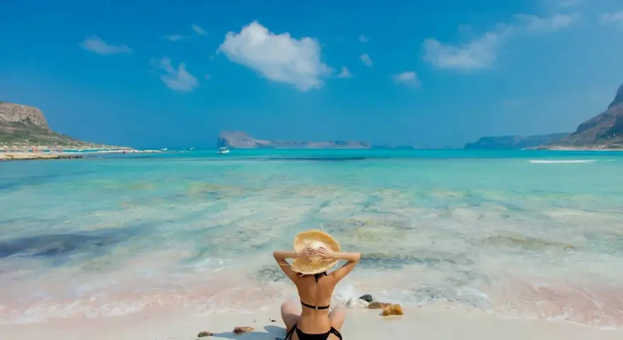 Giovane donna con cappello di paglia ammira il mare turchese, un paradiso tra le isole greche per giovani.