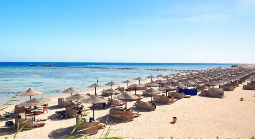 Spiaggia di Marsa Alam con file di ombrelloni e lettini, molo sull'acqua cristallina. Ideale per escursioni e relax.