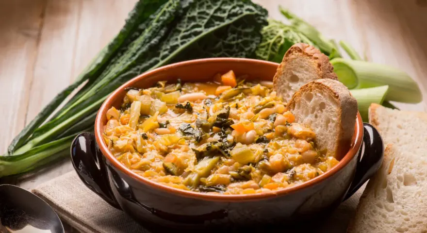 Zuppa di verdure e fagioli, un classico dei cibi tipici toscani, servita con pane rustico e contornata da cavolo nero.