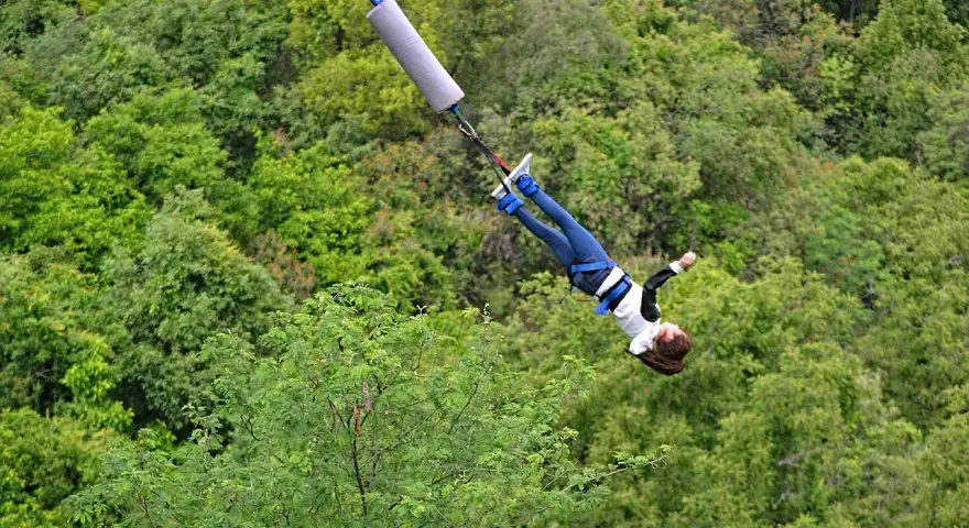 Donna in caduta libera durante un'emozionante esperienza di bungee jumping in Italia, circondata da una lussureggiante foresta verde.