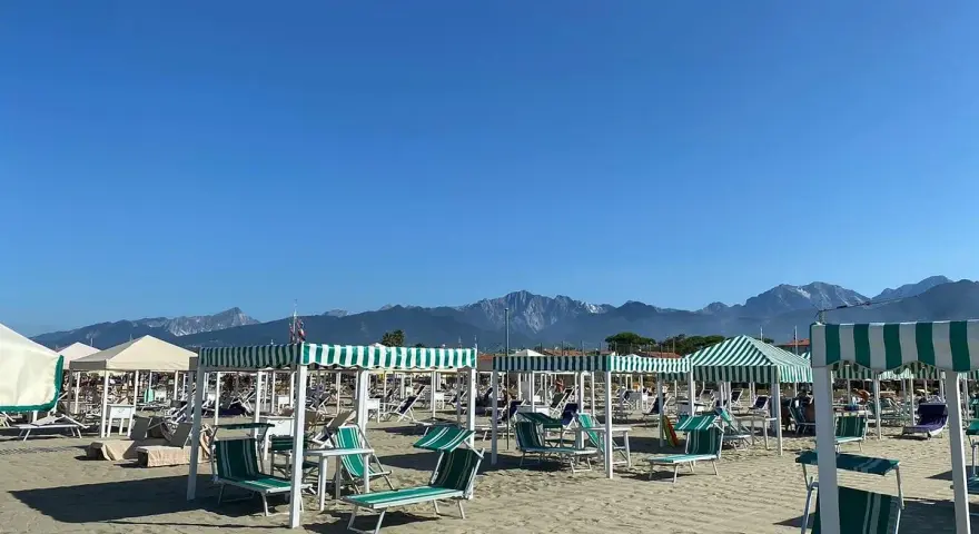Spiaggia attrezzata a Marina di Pietrasanta con lettini e ombrelloni a righe verdi e bianche, sullo sfondo le montagne.